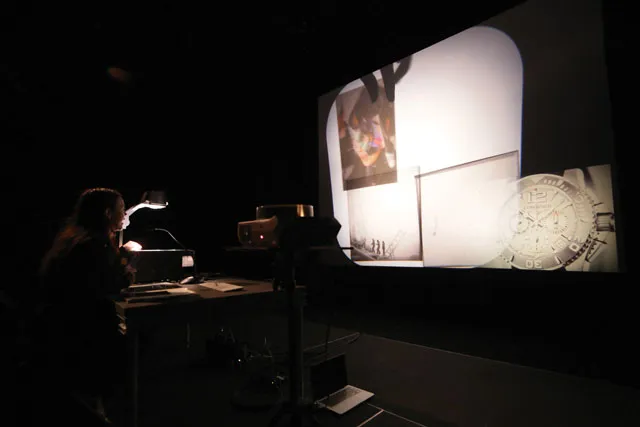 A woman working an overhead projector in a dark room, projecting four random images onto a large screen. 