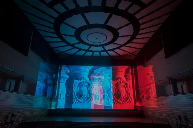 Images of ornate corinthian style columns projected on the back wall of the concert hall in blue and red light. 
