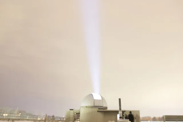An open observatory shooting a beam of light into a gray sky. 