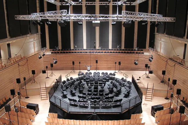 Black folding chairs arranged in a multi ring circle on a constructed black stage in the concert hall orchestra pit. 