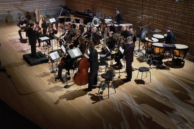 An orchestra dressed in black playing in the concert hall stage. 