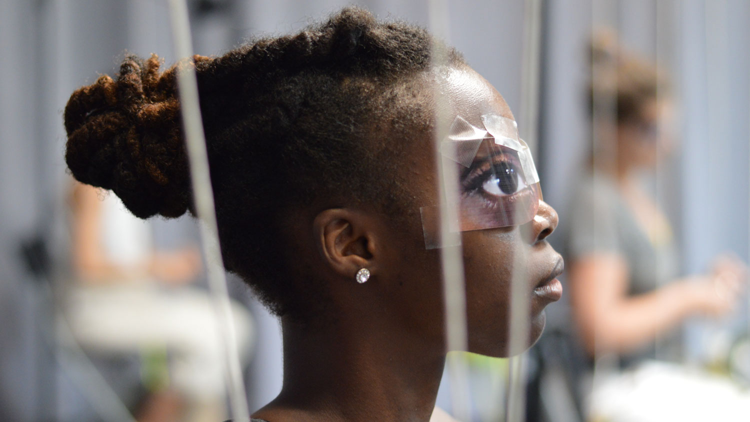 A young Black woman's profile with paper eyes taped over her eyes. 