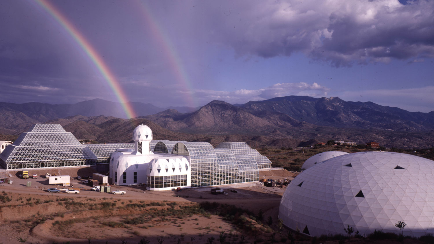 A futuristic town of biospheres in a desert plain with a double rainbow in the sky. 