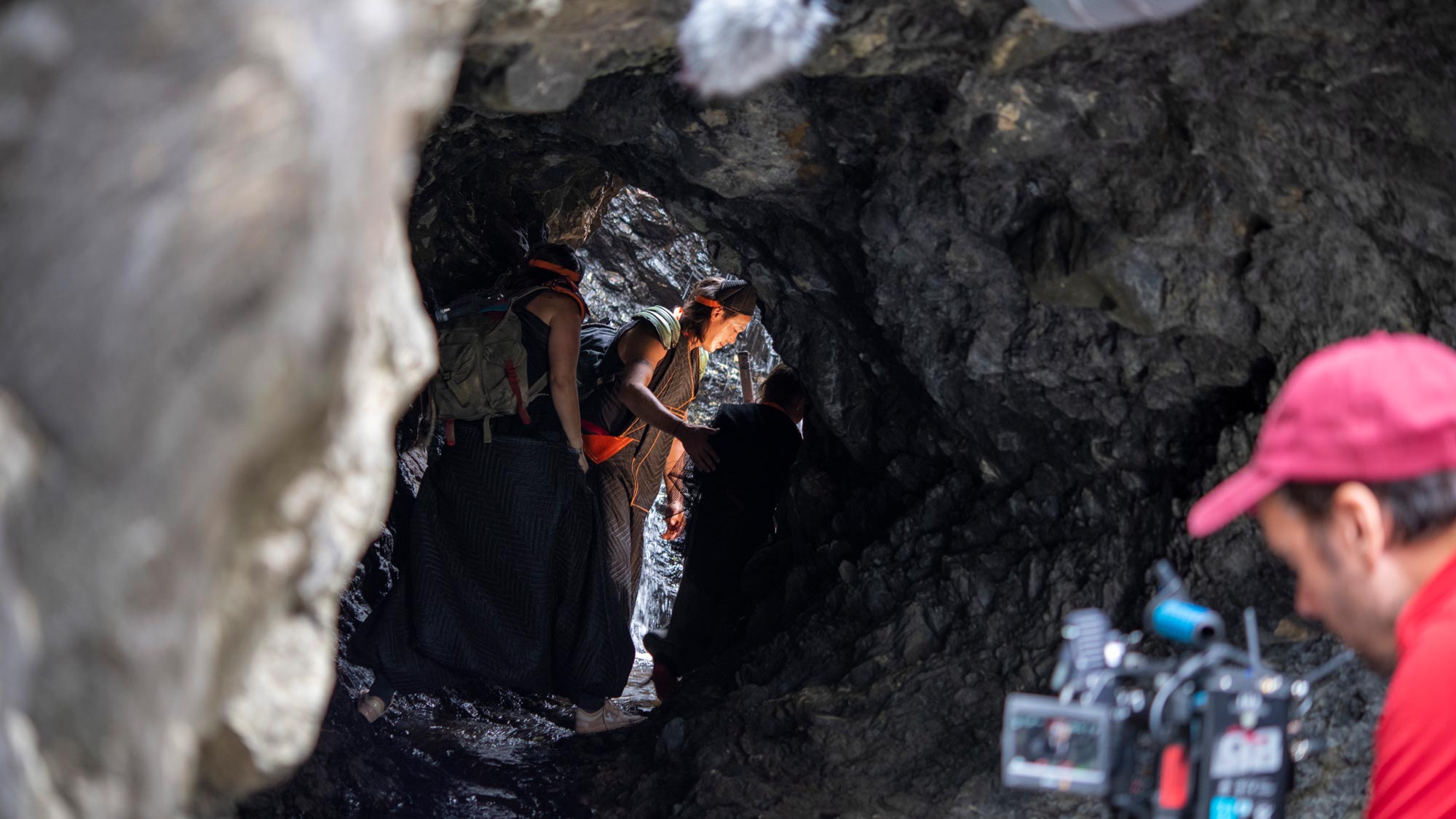 a camera person in the foreground directs a young child and adult in a cave 