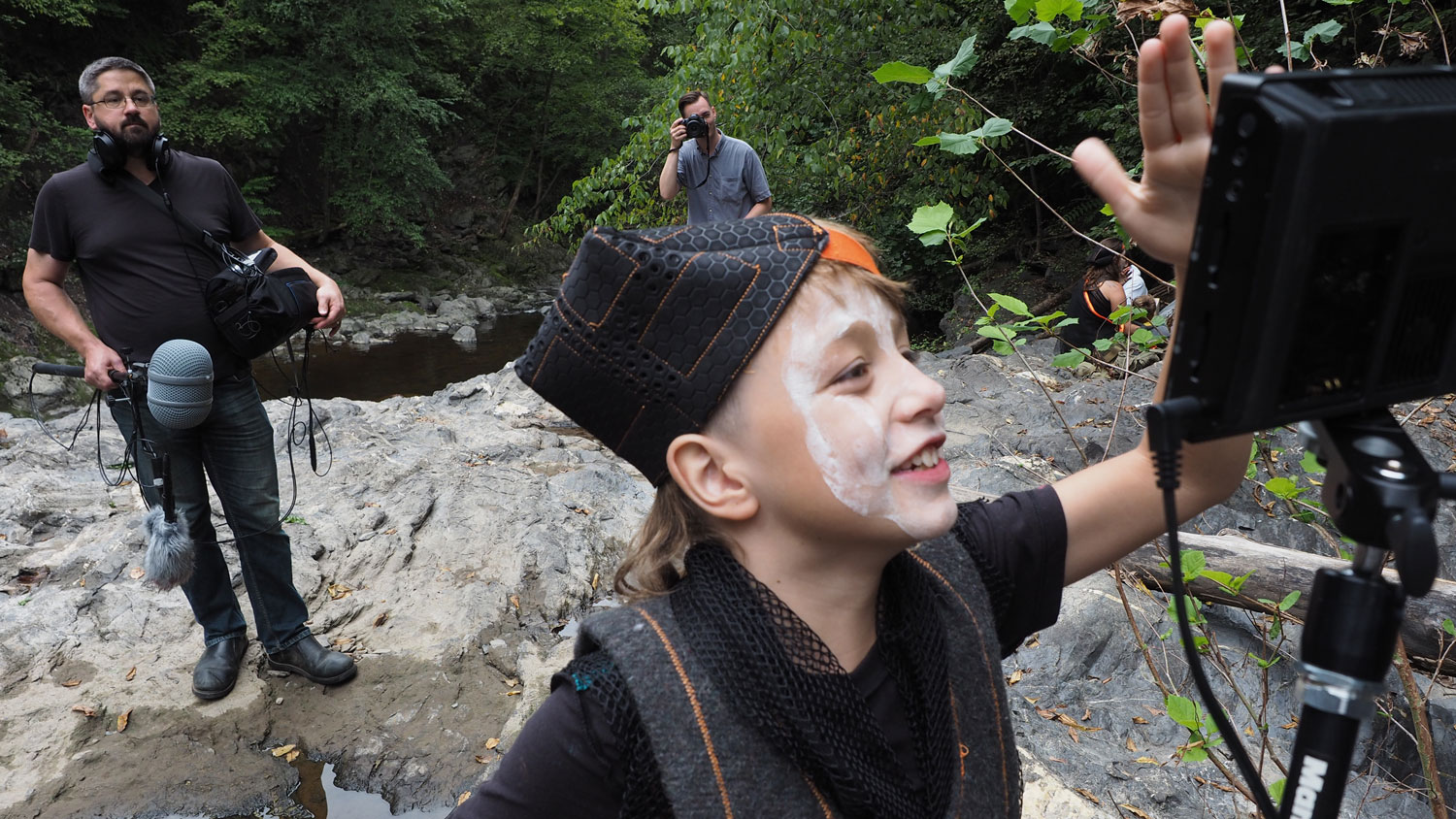 a child looking at a video monitor in a rocky gorge with sound and camera people in the background.