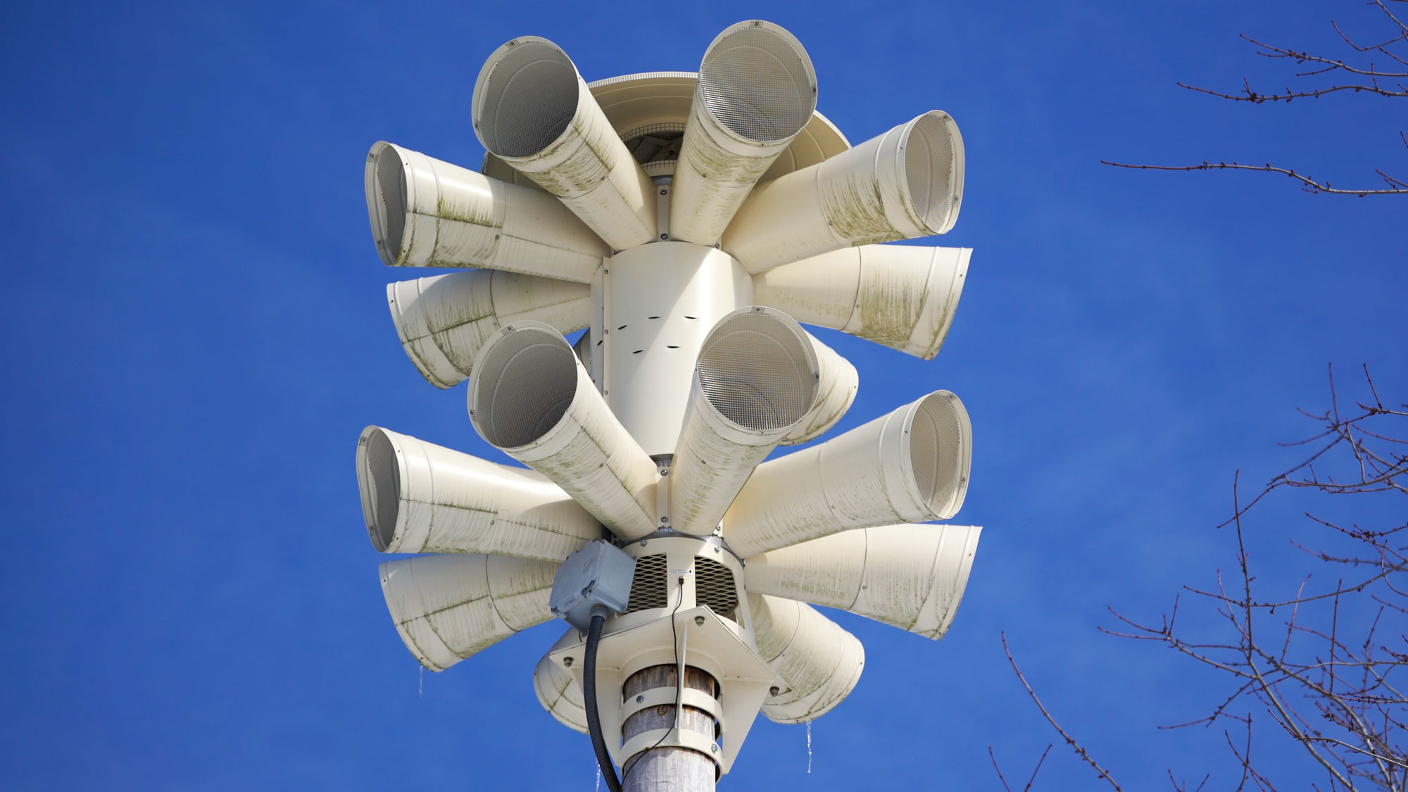 a group of conical loudspeakers atop a white pole against a blue sky