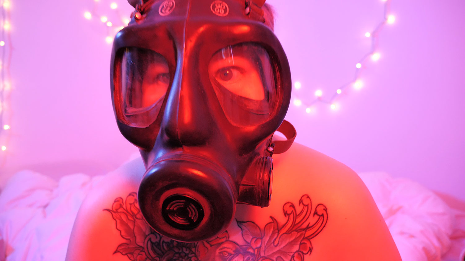 a shirtless tattooed person in a gas mask