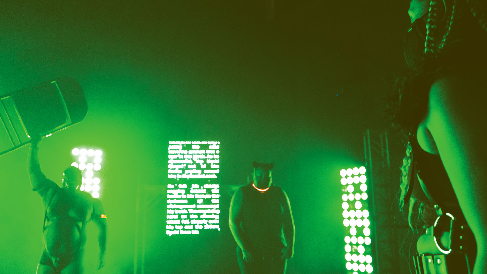 a group of black persons in bondage gear standing in a room lit with grass green light