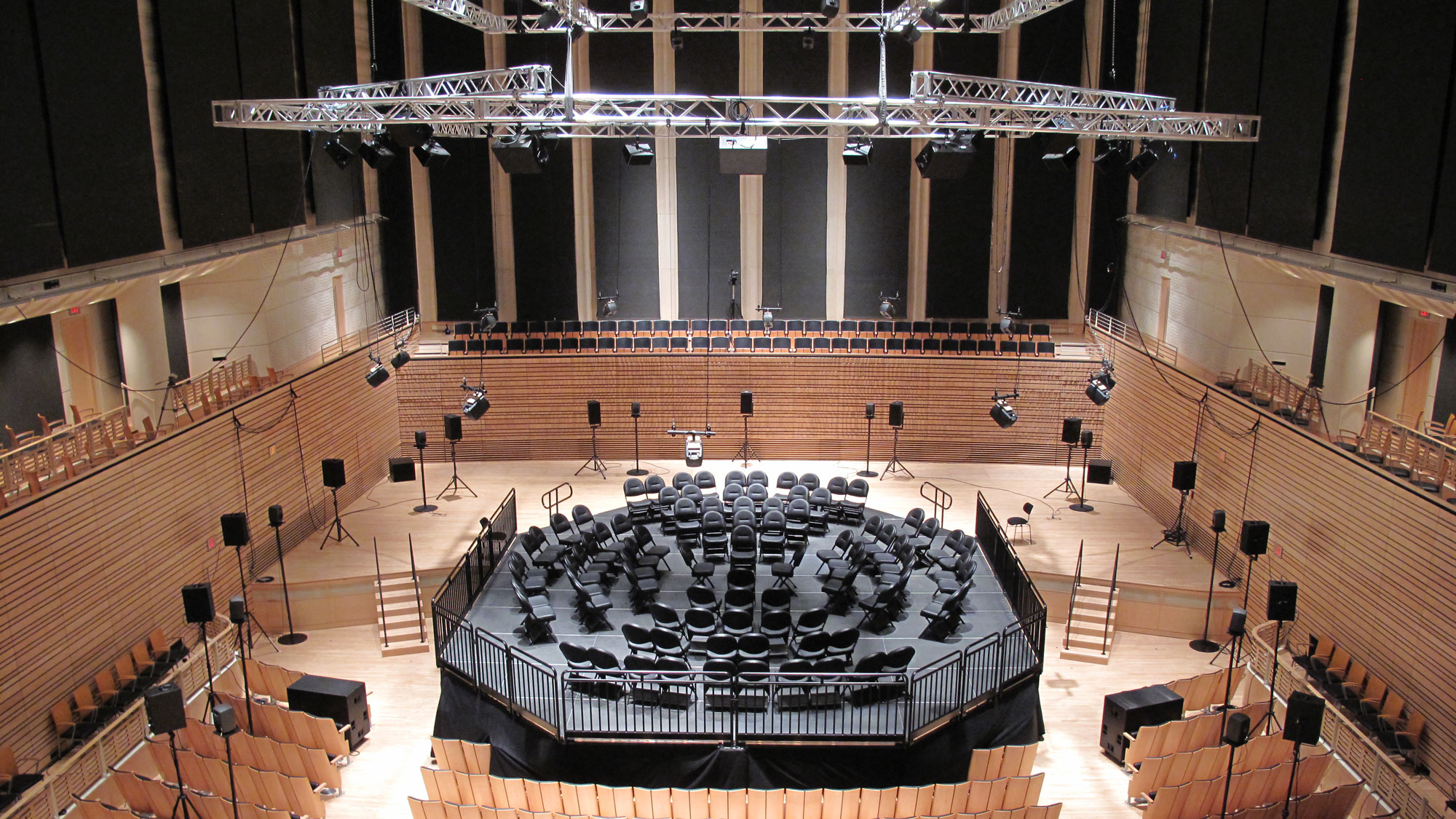 Black folding chairs arranged in a multi ring circle on a constructed black stage in the concert hall orchestra pit. 