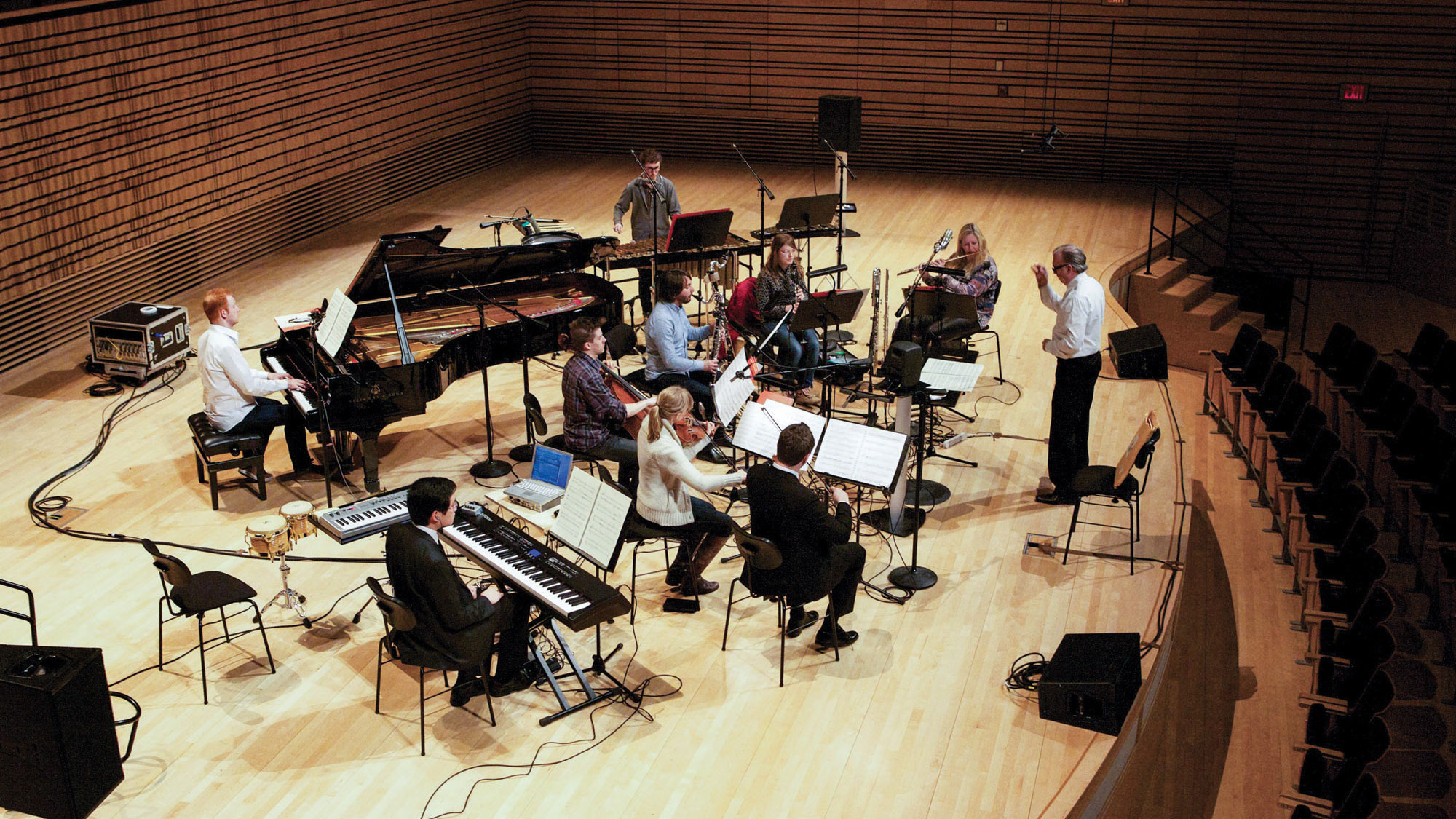 An aerial view of a small orchestra dressed casually in rehearsal on the concert hall stage