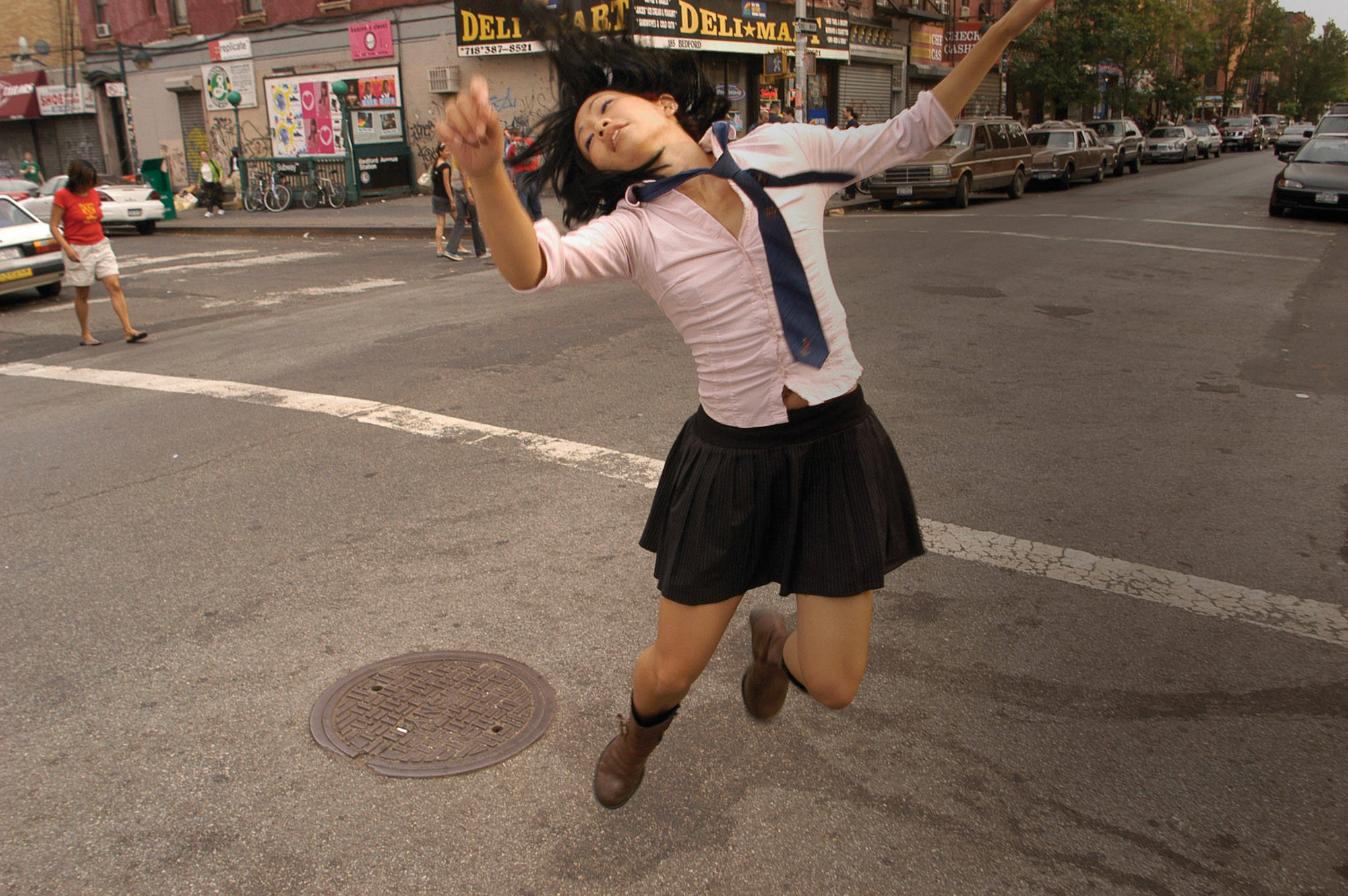 An asian woman wearing a school girl uniform jumping in a city street. 