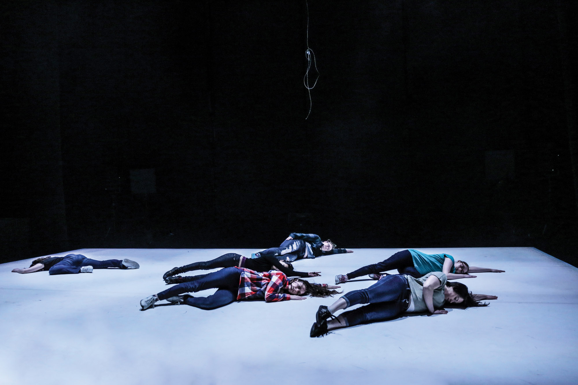 Six dancers laying on a light gray floor. 