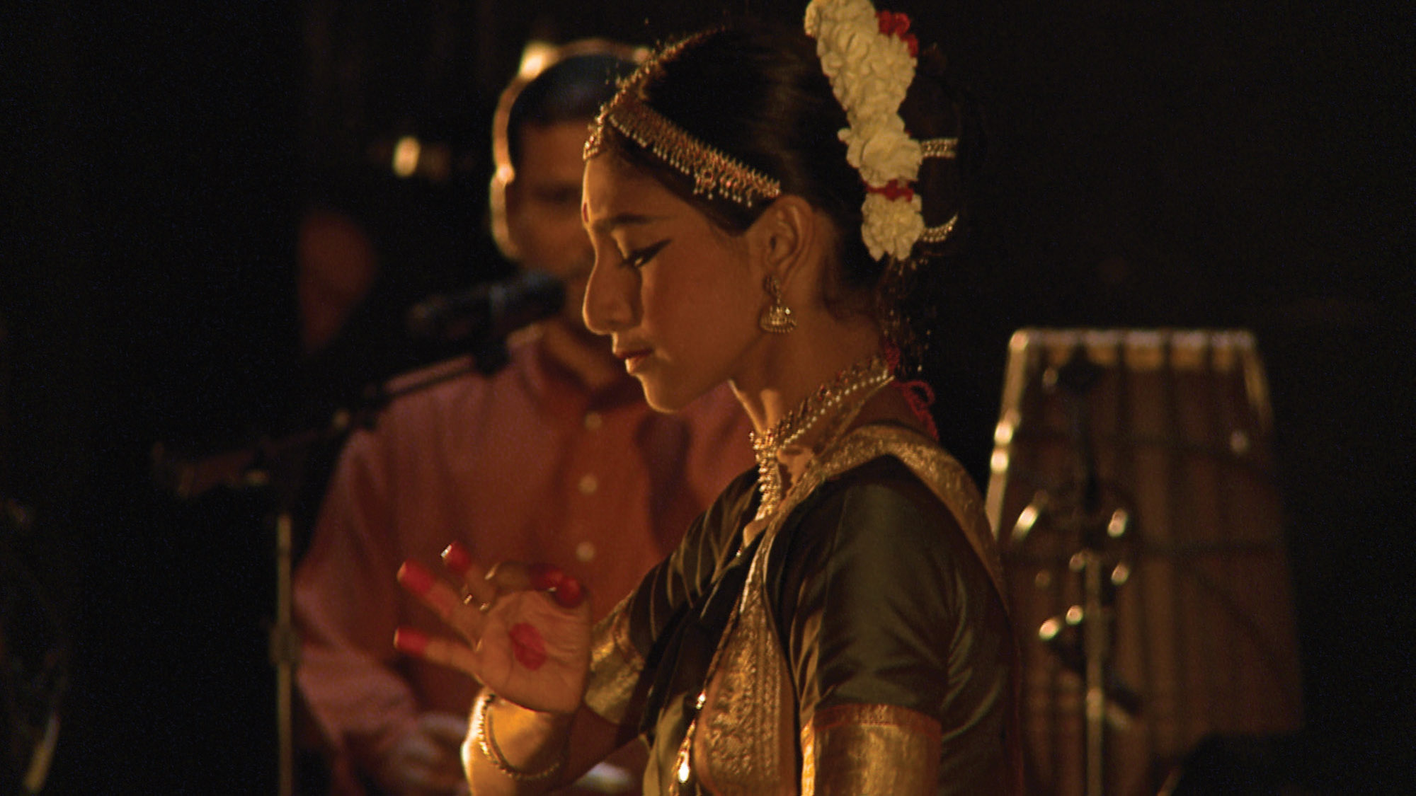 The profile of Indian woman dressed in traditional dress with white flowers in her hair, in a pose, mid dance. 