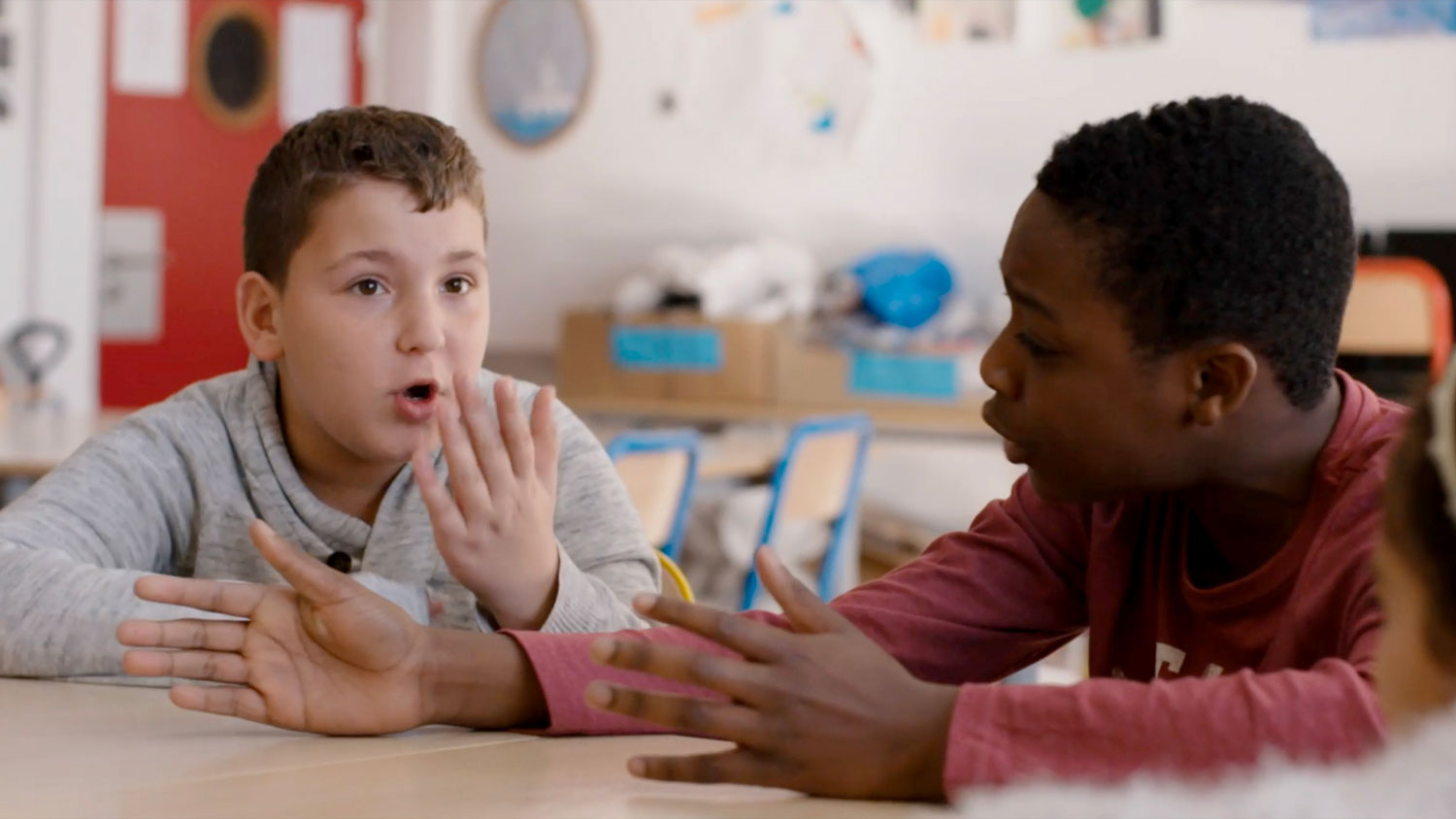 Two young boys seating in an elementary school classroom in active and animated discussion. 