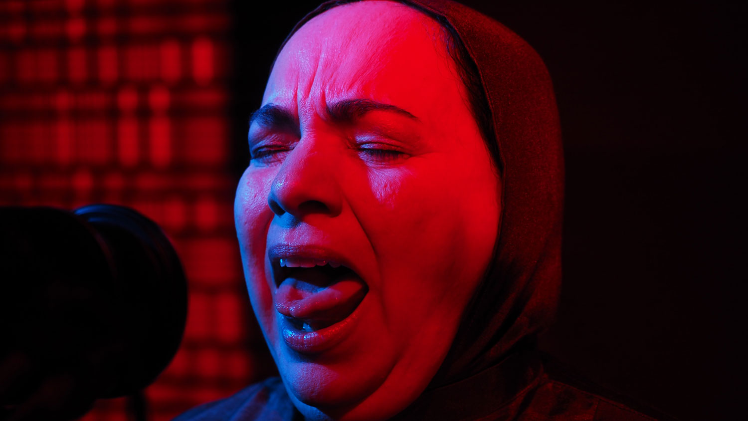 a muslim woman singing into a microphone washed in red light. 