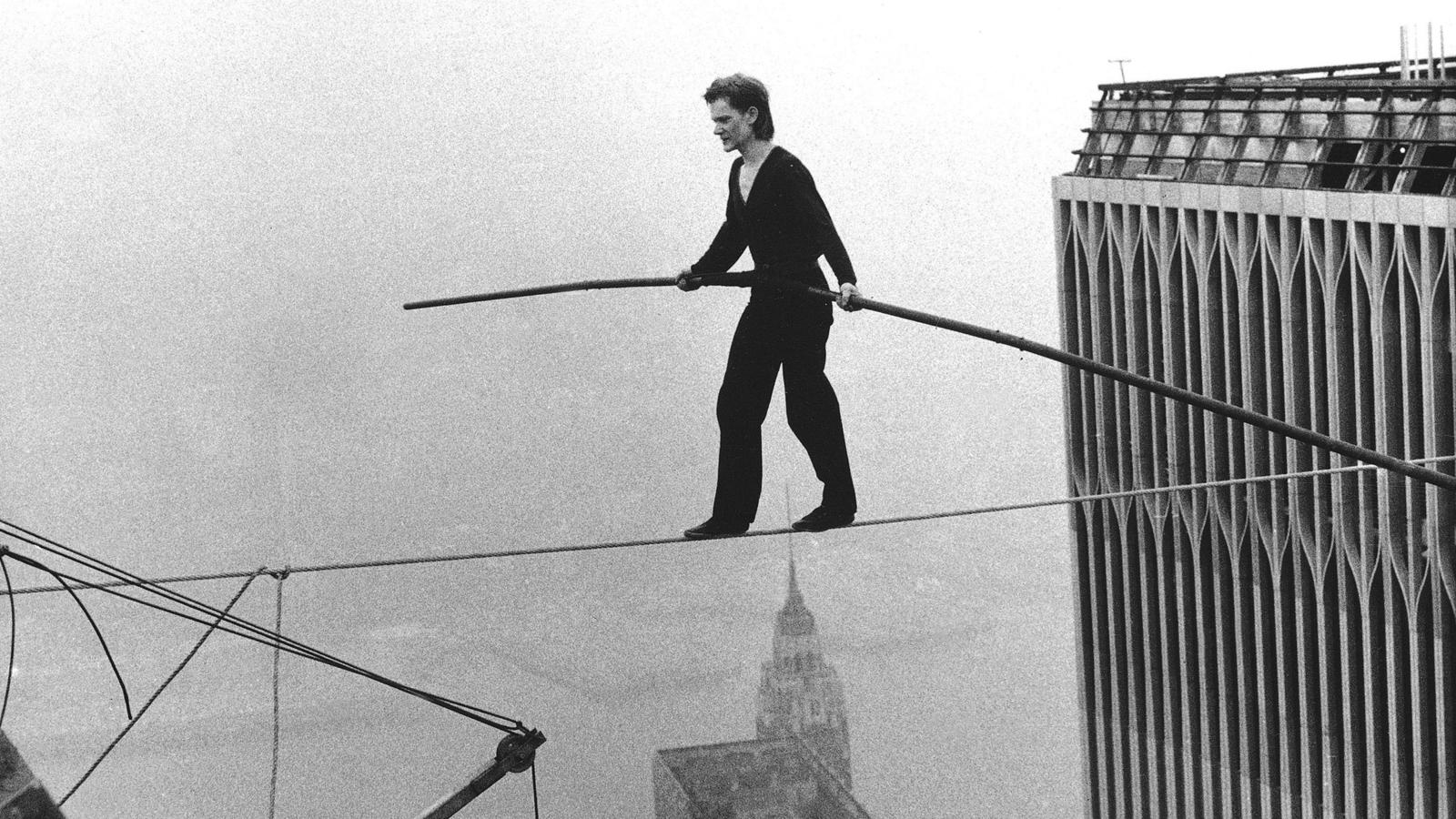 A man wearing a unitard walking across a tight rope spanning between the World Trade Centers. 