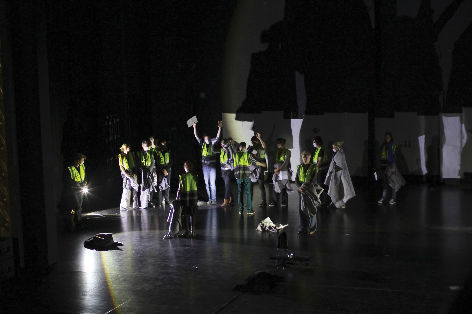 A small crowd of people wearing neon yellow construction vests gathered on a dark stage it only by a flashlight. 