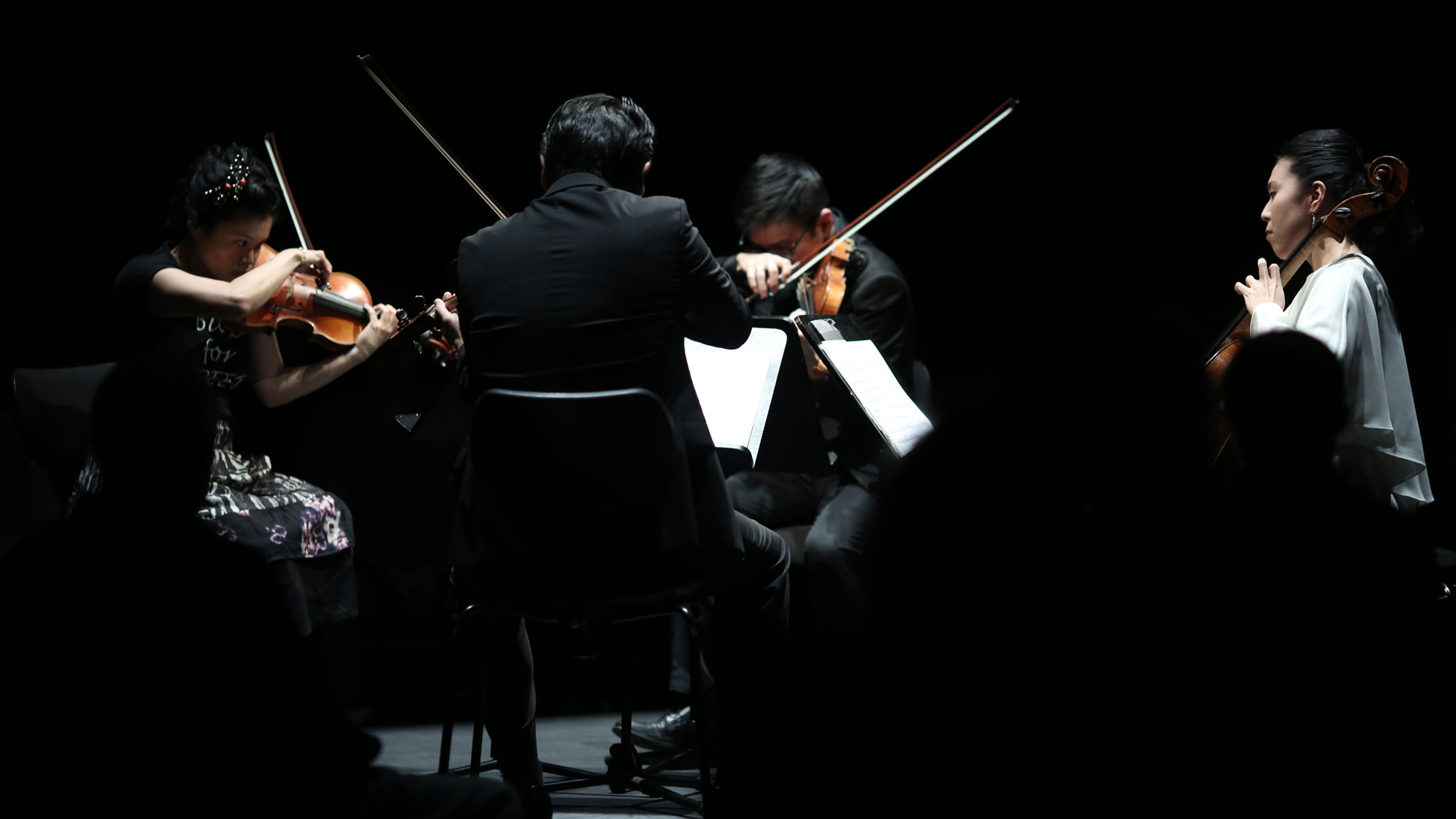 Formosa Quartet actively playing in concert under a spotlight on a dark stage. 