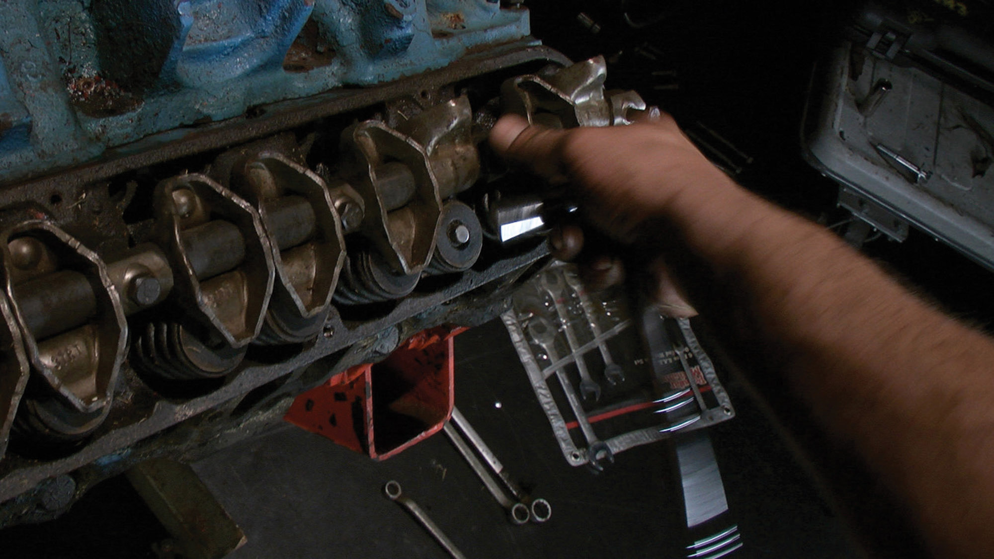 A hand in blurred motion inspecting or repairing the rocker assembly in the cylinder head of an engine. 