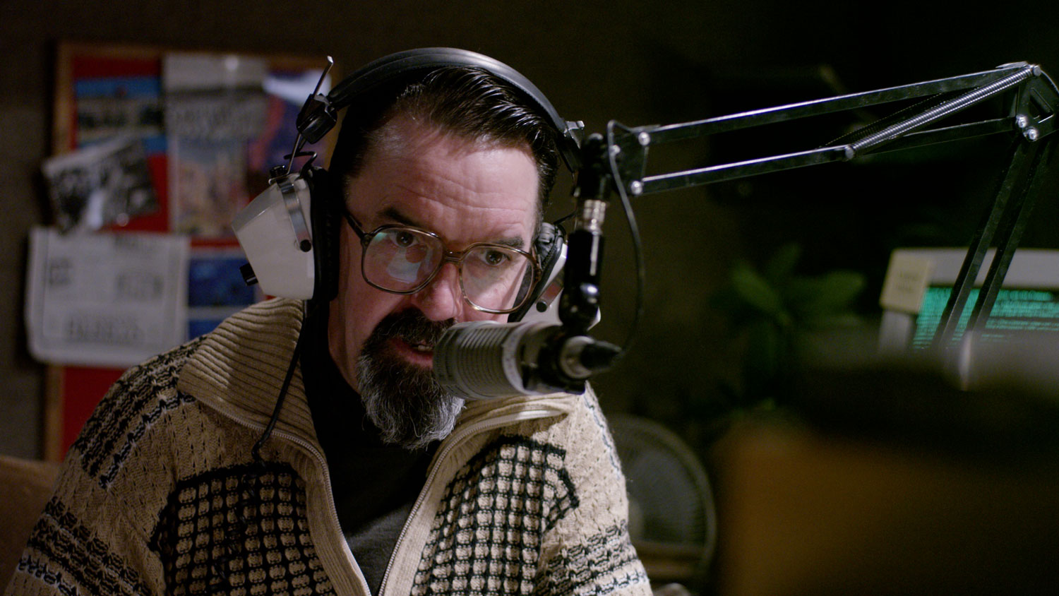 Gerard Byrne speaks into a 70's era radio microphone while wearing white vintage style headphones. 