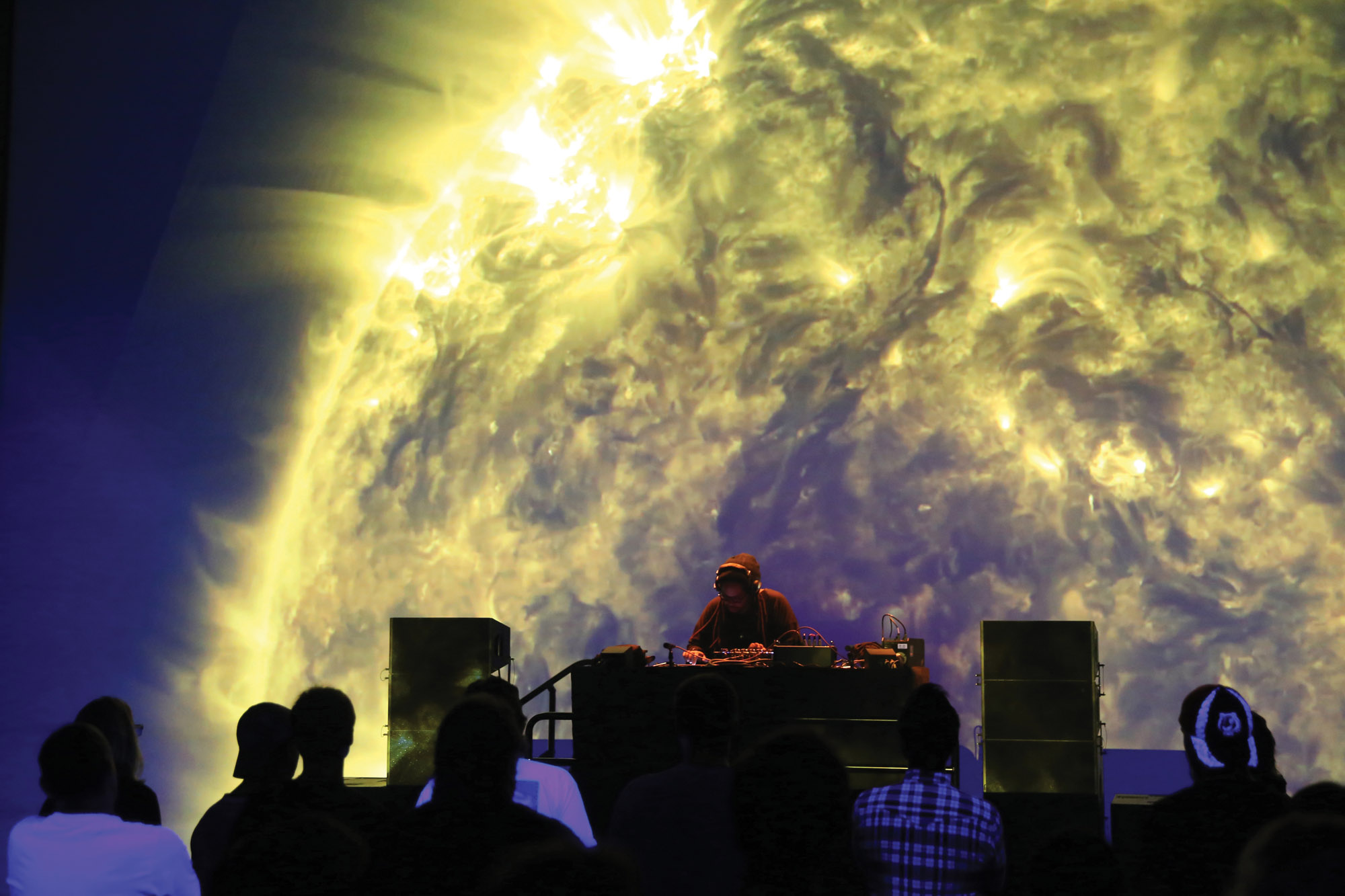 Heiroglyphic Being the artist Doing on stage to a small crowd as an image of the suns solar flares is projected behind him. 