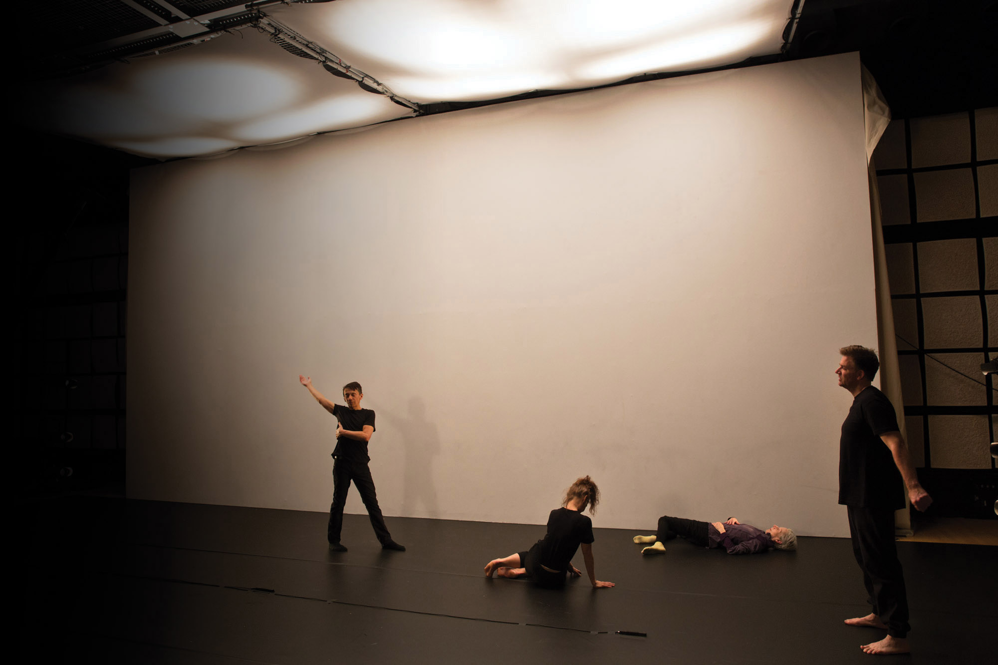 Four dancers stretching before rehearsal in front of a large blank white wall. 