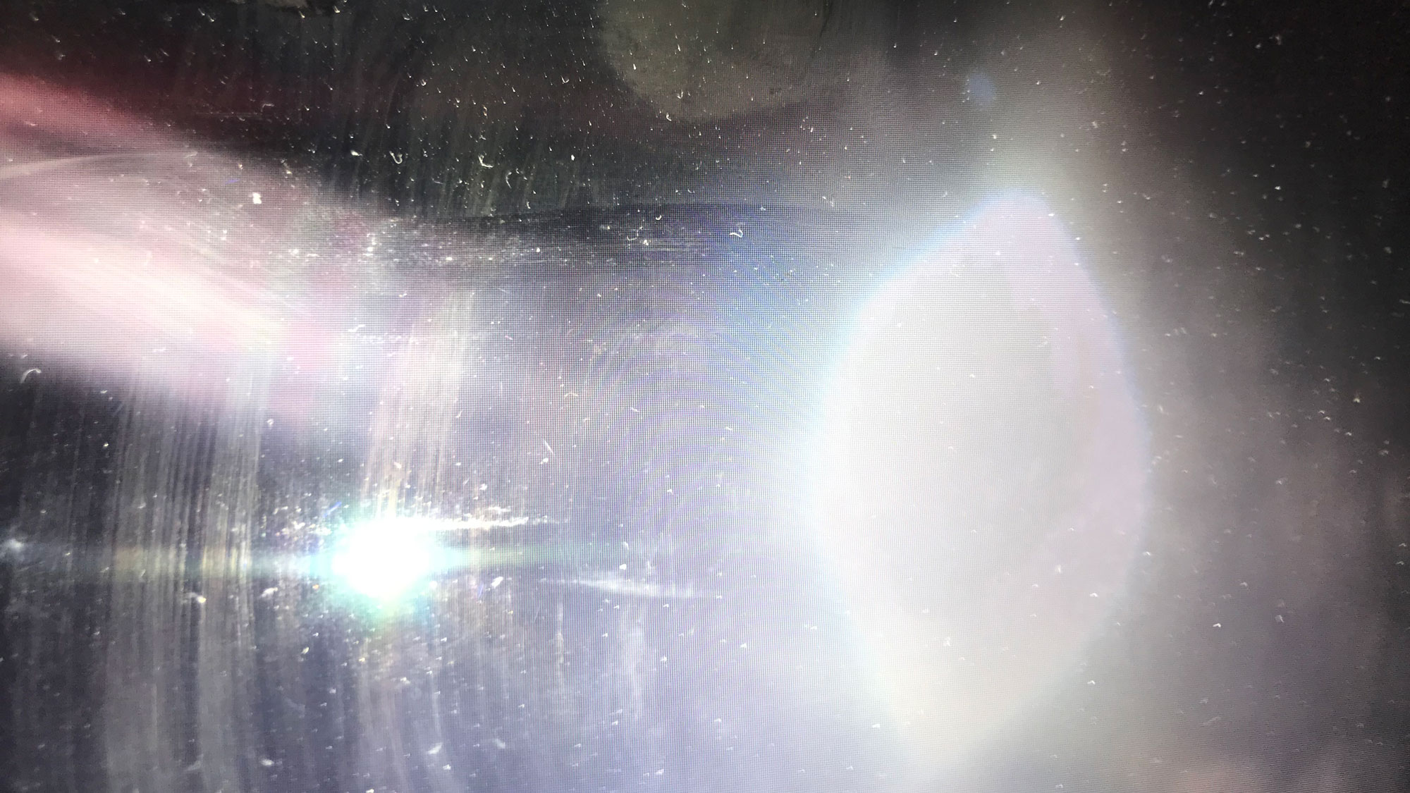 A white light, oval shaped lens flare through a dirty pane of glass.