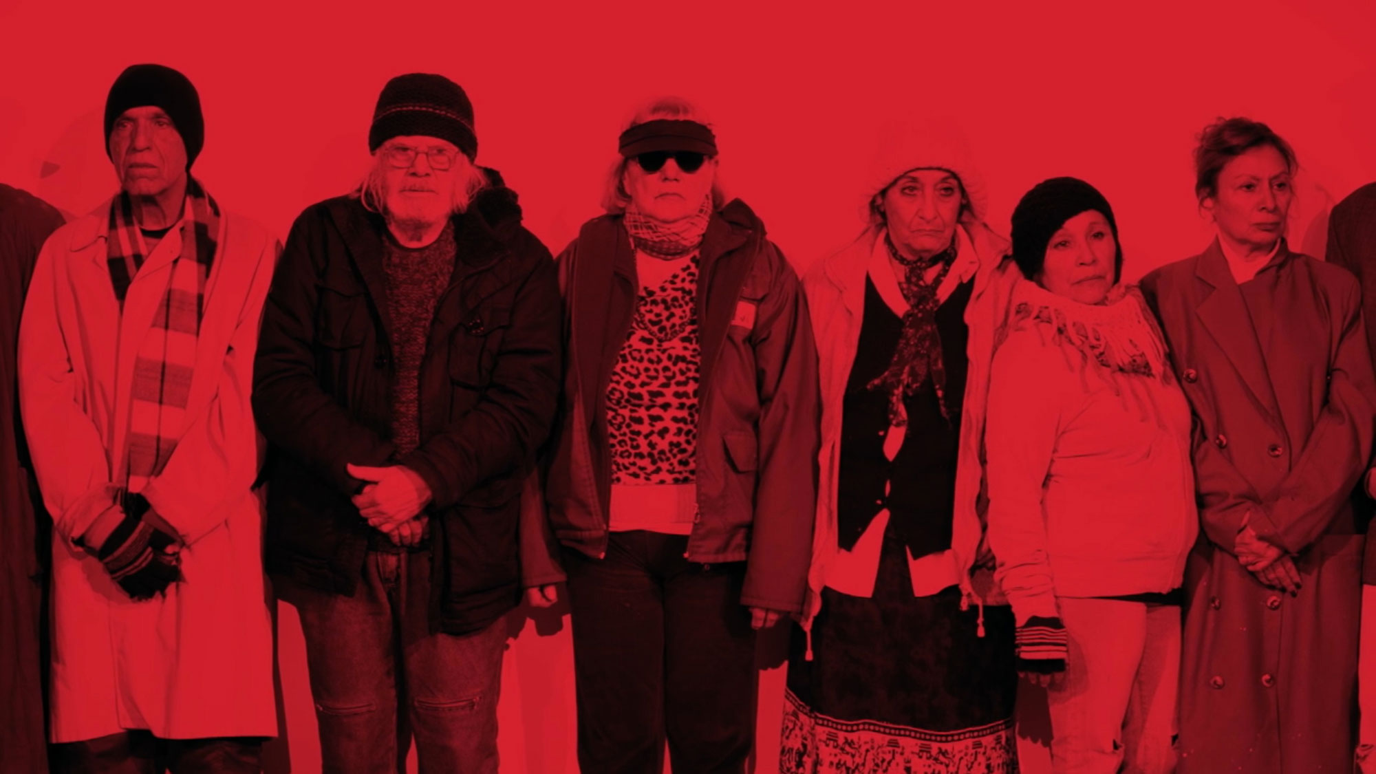 a group of six people bundled in layers of winter clothes washed in red light. 