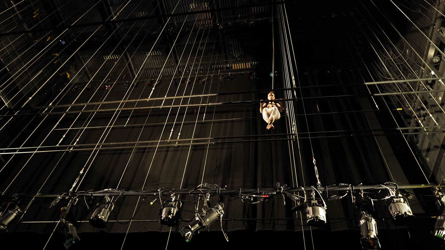 A dancer hanging like a gymnast 40' up among the fly tower line sets oh a black box theater. 
