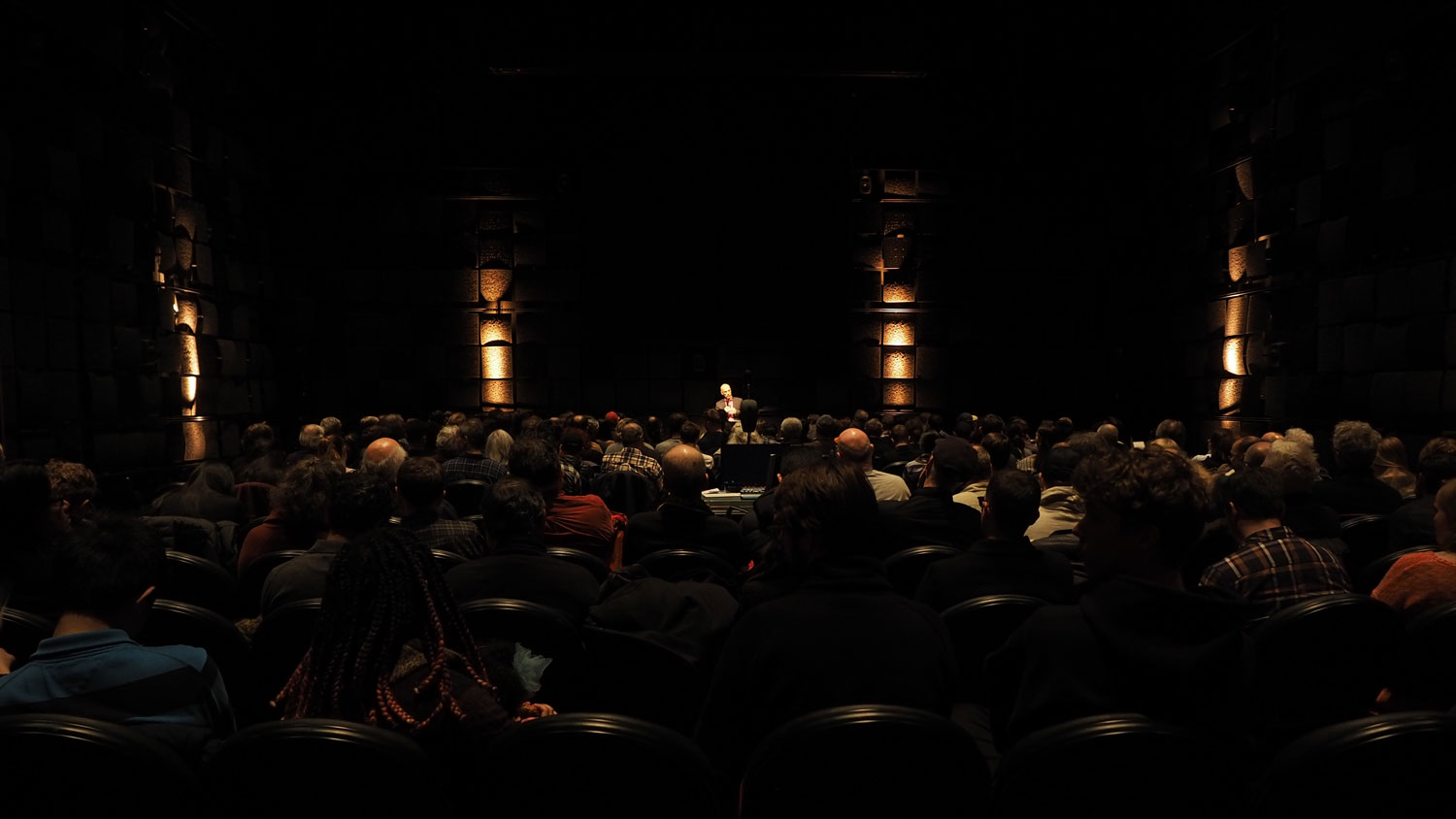 Hans Tutschku giving a lecture to a large crowd in a dark room. 