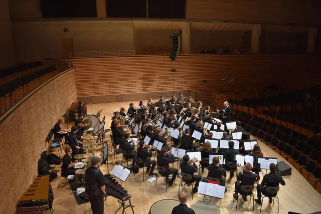 An orchestra seated in a semi circle in dress rehearsal in an empty concert hall. 