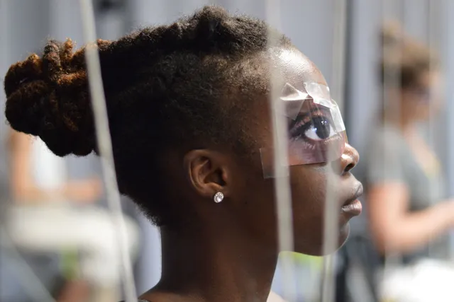 A young Black woman's profile with paper eyes taped over her eyes. 