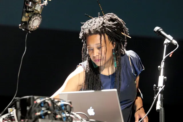 PamelaZ reaching across a lap top next to a microphone focused on the task in front of her.