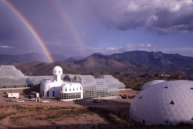 A futuristic town of biospheres in a desert plain with a double rainbow in the sky.