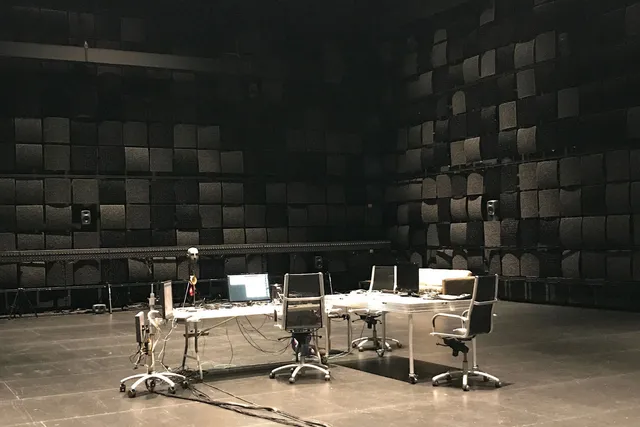 A cluttered conference table with three chairs in the middle a black box theater. 