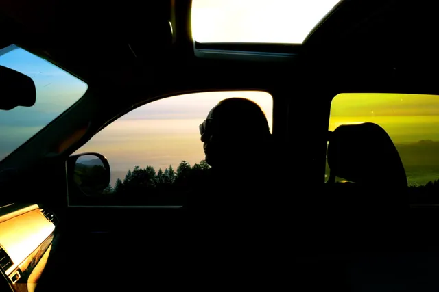 A person silhouetted in the passenger side of a car with the window and sunroof open 