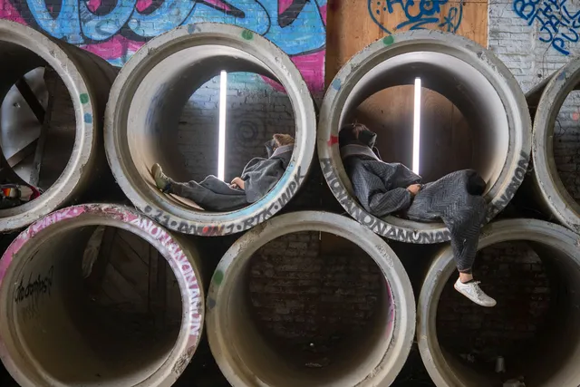 two people laying inside concrete water pipes against a graffiti wall