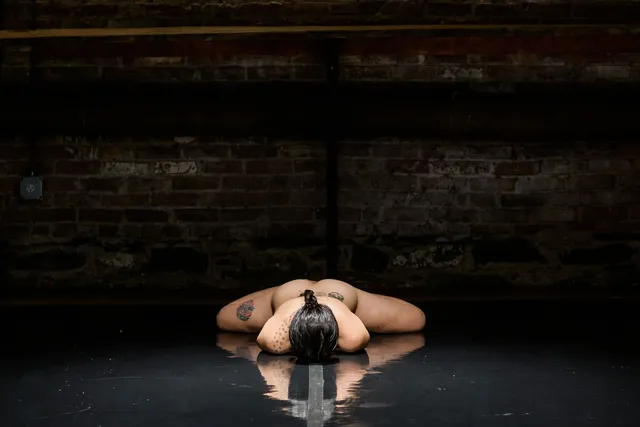 a nude woman on a black stage laying face down with arms under her body