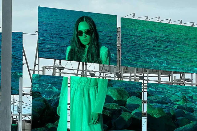 an asian woman in a green tint printed across two city billboards, with ocean shore in the background.