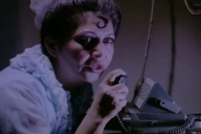 An Afghan woman dressed in 1960's clothing speaking into a CB radio with a distressed look on her face. 