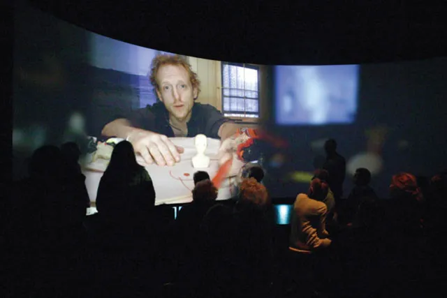 A 360 degree panoramic screen showing a an with red hair reaching as a small crowd gathers in the foreground. 