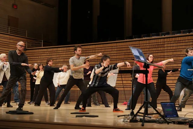A group of people practicing tai chi with laurie anderson on EMPAC's concert hall stage.