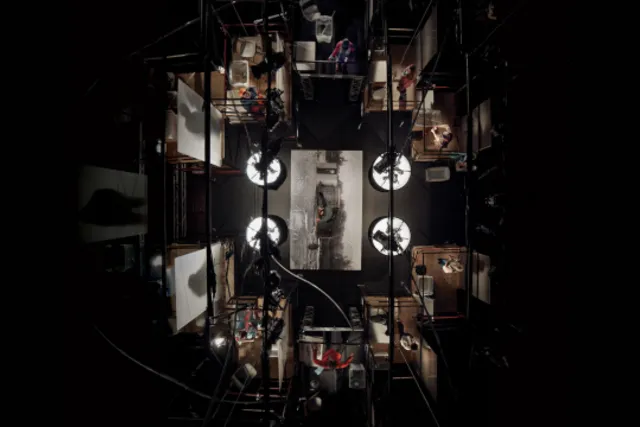 An aerial view looking through the rigging above a black box theater down on multiple people working in various sets. 