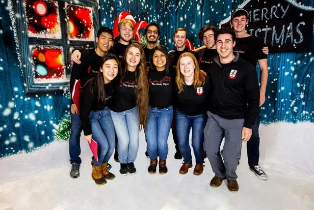 A group of 11 students wearing black tops and jeans posing in a snowy, holiday scene. 