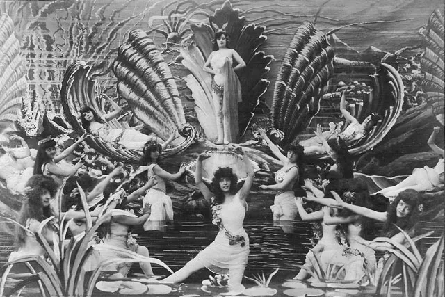 A 20's film still of about thirteen woman dressed as water nymphs posed on different tires of a set. 