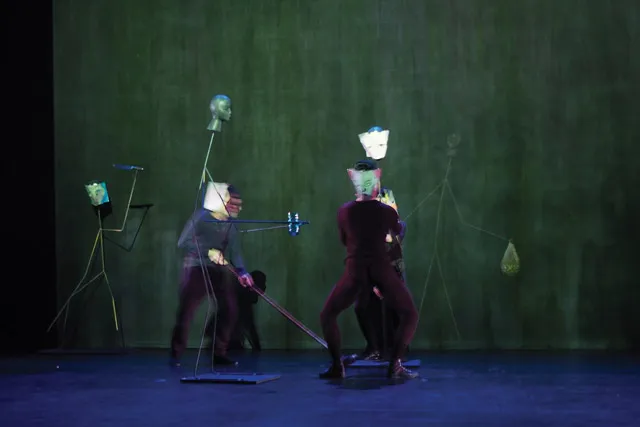 Two performers in black manipulating an assortment of human-esque sculptures.