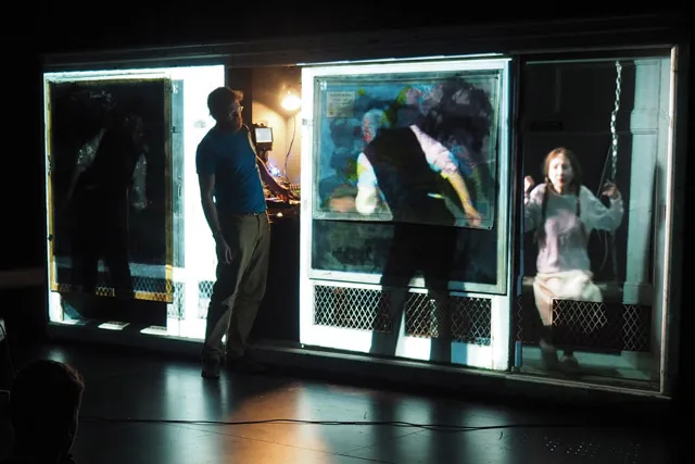 A contemporary man with a beard looking at a projection of a victorian era man and young girl projected over panes of glass.