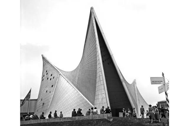 A man made cave type structure with a pointed roof and covered in glass. A small crowd looks on with backs to the camera.