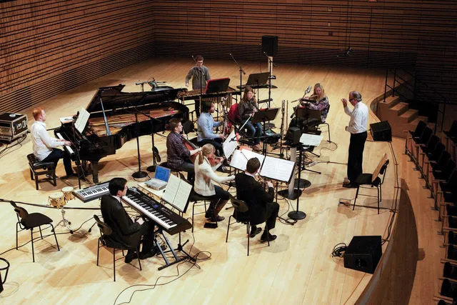 An aerial view of a small orchestra dressed casually in rehearsal on the concert hall stage