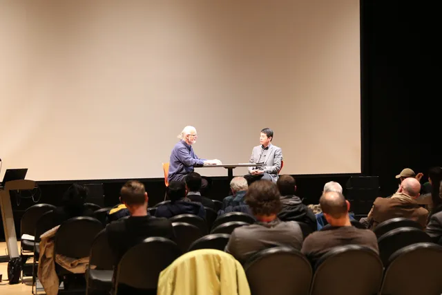 Johannes Goebel and Hui Su in discussion in front of a seated crowd. 